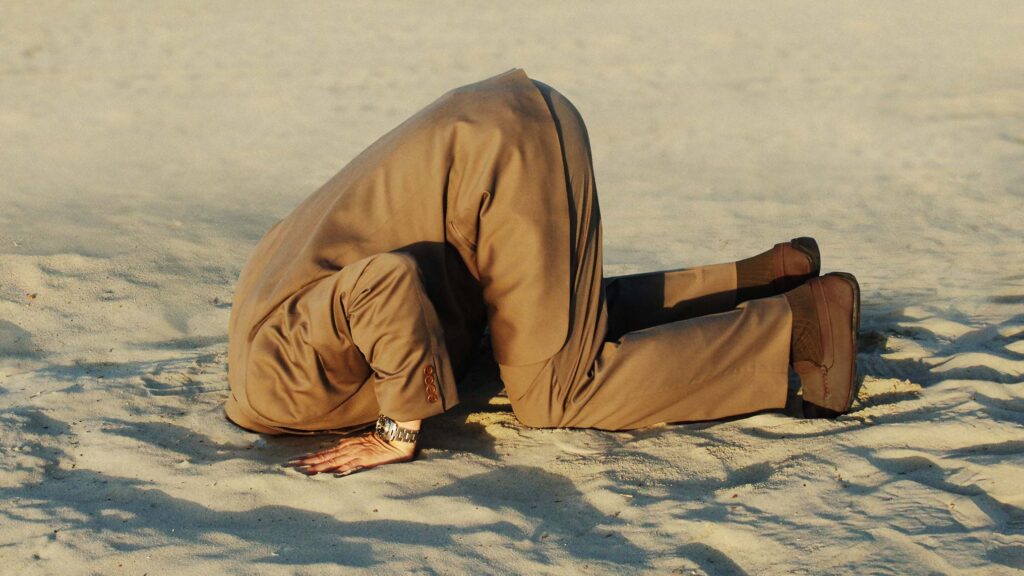 Image of a guy in a business suit with his head buried in the sand.
