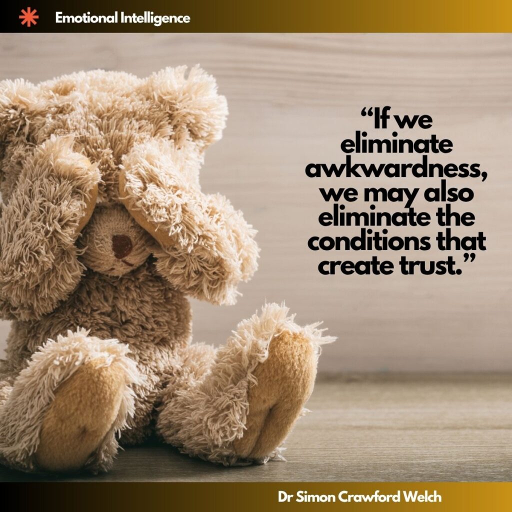 A worn, weathered teddy bear sitting alone with its head bowed against a pale wooden background, evoking vulnerability and the discomfort inherent in authentic human connection. The concept highlights how emotional intelligence requires tolerating awkwardness as a necessary pathway to building genuine trust. "If we eliminate awkwardness, we may also eliminate the conditions that create trust." By Dr. Simon Crawford Welch
