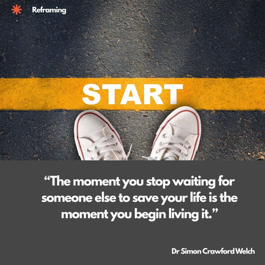 A pair of white canvas sneakers photographed from above stands on dark asphalt just behind a thick yellow line marked START. The concept is the decision point, showing that beginning is a place you step over rather than wait beside. Text over the image reads: "The moment you stop waiting for someone else to save your life is the moment you begin living it." By Dr Simon Crawford Welch.