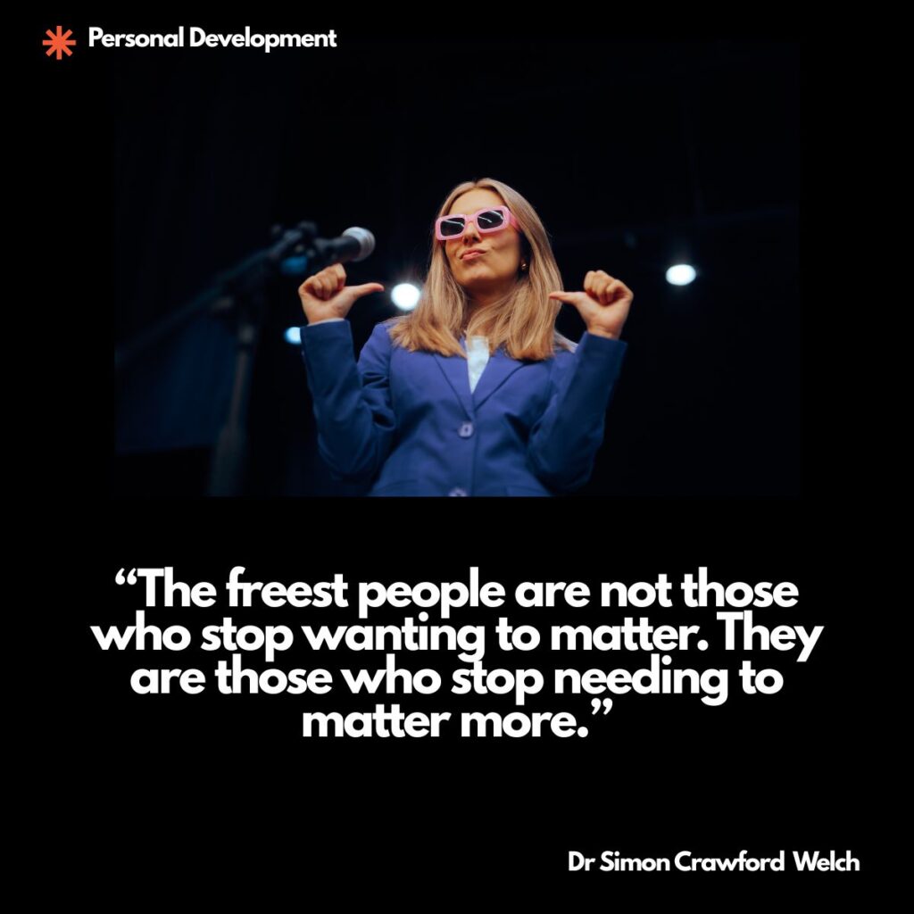 A woman in a bright blue blazer and pink sunglasses stands on a dark stage beside a microphone, smirking and pointing both thumbs at herself under the spotlights, with a Personal Development label in the top corner. The image represents the hunger to be the center of every room and the freedom of no longer needing to be. Quote over the image reads: "The freest people are not those who stop wanting to matter. They are those who stop needing to matter more." By Dr. Simon Crawford Welch.