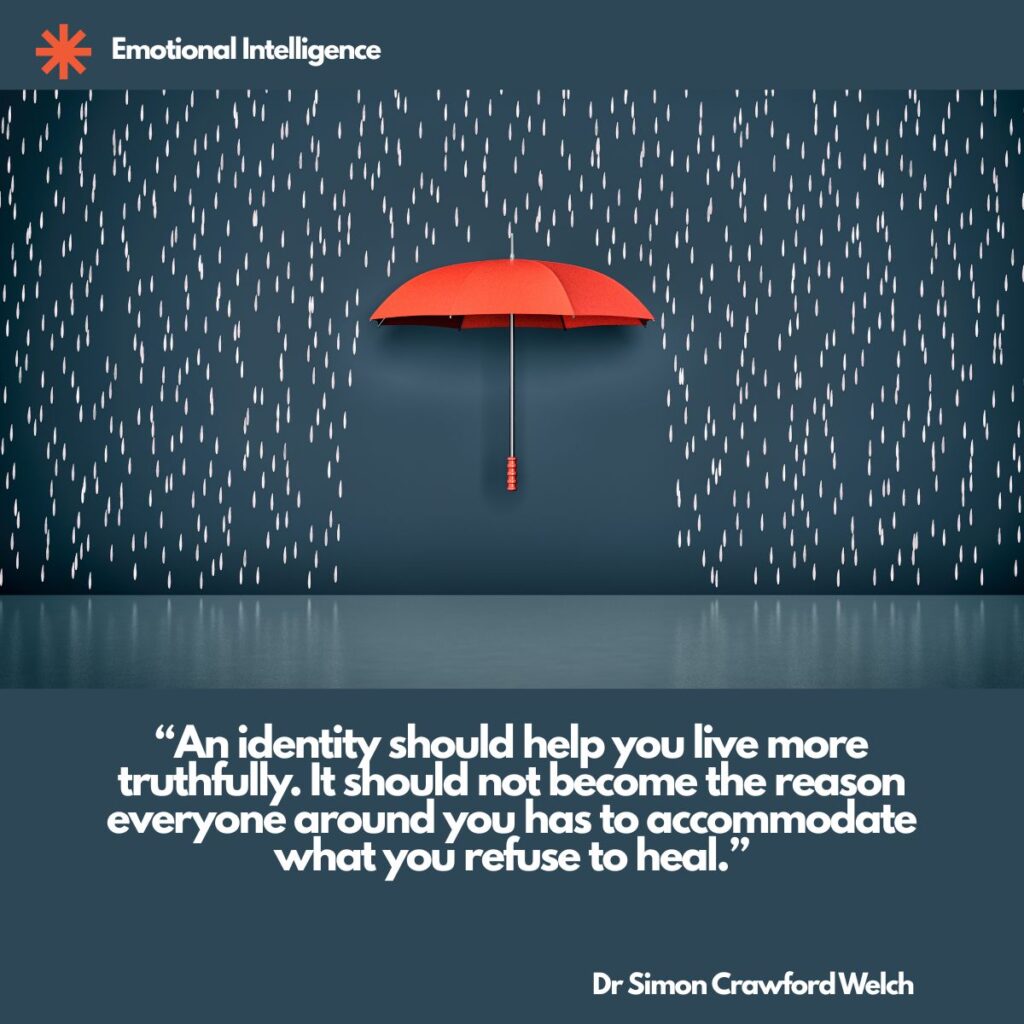 A single red umbrella floats open against a dark teal wall as white raindrops fall on either side of it, leaving the space beneath the umbrella dry, with an Emotional Intelligence label in the top corner. The image represents an identity used as shelter rather than as a way of living more truthfully. Quote over the image reads: "An identity should help you live more truthfully. It should not become the reason everyone around you has to accommodate what you refuse to heal." By Dr. Simon Crawford Welch.