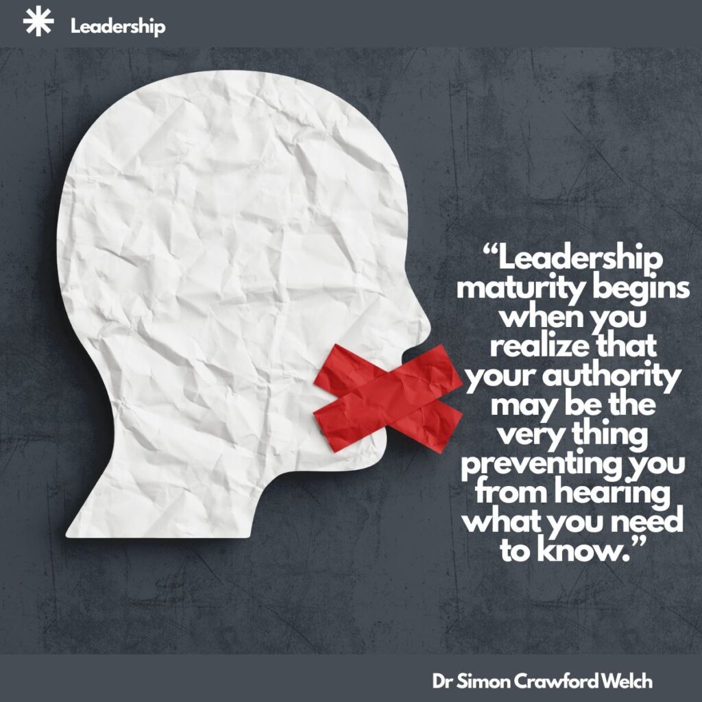 A white crumpled paper cutout of a human head in profile has a red tape X over its mouth, set against a dark slate grey textured background, with a Leadership label in the top corner. The image represents the silence that forms around leaders when people stop telling them the truth. Quote over the image reads: "Leadership maturity begins when you realize that your authority may be the very thing preventing you from hearing what you need to know." By Dr. Simon Crawford Welch.